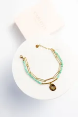 Pulsera dorada de doble cadena, una de eslabones y otra de cuentas facetadas color verde agua. Dije circular texturizado con una pequeña piedra central.
