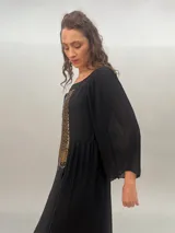 Vestido largo de gasa negra con estampado abstracto color dorado. Presenta mangas largas plisadas, escote cuadrado, tajo lateral y forro interior.