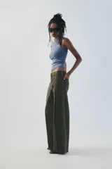 Pantalón verde militar de tiro medio, con bolsillos delanteros, pliegues y tejido con efecto lavado. Cuenta con cierre frontal con cremallera y gancho metálico.