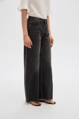Pantalón jean gris de tiro alto, corte ancho (wide leg) con diseño de paneles tipo patchwork y terminación desmechada en el dobladillo.