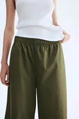 Pantalón de algodón color verde militar, de corte ancho y tobillero. Presenta cintura elástica fruncida y piernas amplias.
