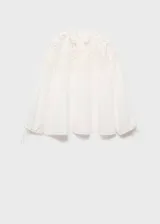 Blusa blanca de corte recto con cuello redondo y tiras para lazo. Presenta detalles bordados calados en la parte superior y mangas largas con terminación en lazo.