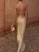 Vestido largo de satén color dorado, de silueta fluida, con espalda descubierta, tiras finas cruzadas y aplique decorativo con brillos.