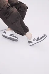 Zapatillas de diseño urbano en color blanco con inserciones en gris oscuro, cordones al tono y detalle de estrella bordada en el lateral.