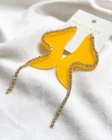 Par de aros colgantes de acrílico amarillo con forma abstracta y borde de strass plateado. Cierre de gancho.