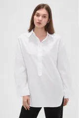 Camisa blanca de algodón, de corte holgado, manga larga con puños anchos y cuello camisero. Cuenta con cierre frontal parcial de botones.