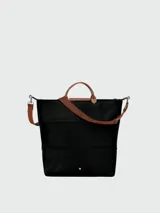 Bolso de viaje Longchamp modelo Le Pliage Original, de diseño ampliable, confeccionado en nylon negro con detalles en cuero marrón en las asas y solapa frontal con cierre de botón a presión. Incluye correa ajustable y extraíble.
