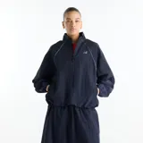 Campera New Balance de dama modelo Sport Legacy, confeccionada en tejido ripstop de nailon reciclado con tratamiento resistente al agua. Diseño en color azul marino, con cuello alto, cierre frontal completo, mangas raglán y bolsillos laterales de ribete con cierre a presión. Cuenta con logotipo NB tonal termosellado en el pecho.