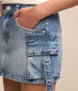 Pollera mini de jean con efecto mármol, diseño de tiro medio con bolsillos cargo laterales, lazos decorativos con hebillas y cierre frontal tradicional.