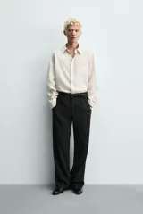Camisa de corte relajado confeccionada en tejido fluido con textura jacquard de rayas verticales. Presenta cuello clásico, cierre frontal con botones, manga larga con puños abotonados y un bolsillo de parche en el pecho.