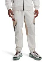 Pantalón cargo técnico de Under Armour, confeccionado en tejido elástico con tecnología UA Storm repelente al agua. Presenta un diseño en tonos beige y blanco con paneles en contraste, bolsillos laterales con cremallera, cintura elástica con cordón interno y bajos ajustables con cordón elástico.