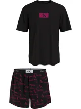 Conjunto de pijama Calvin Klein 1996, compuesto por una remera negra de algodón con cuello redondo, manga corta y logo estampado en el pecho, y un short negro de algodón tejido con bolsillos laterales, cintura elástica con logo y estampado del logo de la marca en color fucsia.