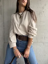 Blusa de color beige con diseño de corte holgado y mangas largas abullonadas. Presenta detalles bordados en tono sobre tono en las mangas y puños ajustados.