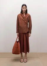 Camisa de algodón color marrón, de diseño cruzado estilo sobre con lazo lateral para anudar, cuello camisero, manga larga y calce amplio.