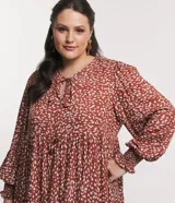 Vestido corto amplio color ladrillo con lunares irregulares color crema, cuello redondo con lazo, mangas largas con puños anchos y bajo fruncido.