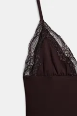 Vestido mini negro con escote en pico y tirantes finos ajustables. Presenta detalles de encaje combinado a tono en el escote y en el ruedo.