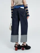 Pantalón de jean azul oscuro de corte ancho, con tiro medio y un marcado doblez en el bajo que deja ver el tono más claro del denim. Presenta costuras en contraste y un diseño de pierna recta.