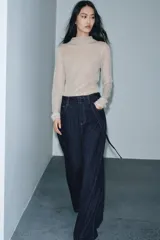 Jeans de tiro alto con pierna ancha, confeccionados en denim azul oscuro. Presentan cinco bolsillos, trabillas en la cintura y un cinturón ajustable del mismo tejido con hebilla metálica. Incluyen pespuntes marcados a tono y cierre frontal con cremallera y botón.