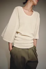 Jersey amplio de punto color beige, con escote redondo y mangas anchas por debajo del codo. Presenta detalles de calados en los laterales.