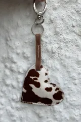 Llavero con dije en forma de corazón confeccionado en cuero con pelo estampado tipo animal print, unido a una argolla metálica mediante una tira de cuero marrón.