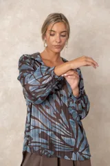 Blusa de gasa con estampado abstracto en tonos verdes y marrones, con detalles de hilos dorados. Presenta cuello camisero con escote en V, mangas largas con puños elásticos y un corte holgado.