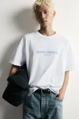 Remera blanca de corte relaxed fit con cuello redondo y manga corta. Presenta un estampado frontal en color celeste con el texto "HOTEL CENTRAL" acompañado de cinco estrellas.