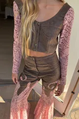 Top corto confeccionado en cuero negro con mangas largas de encaje floral. Presenta escote en V, diseño entallado con costuras decorativas y cierre frontal mediante botones metálicos.