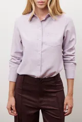 Camisa blanca de manga larga con cuello clásico y botones frontales. Tiene un bolsillo en el pecho con un pequeño logo bordado.