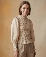 Blusa color verde oliva confeccionada en muselina de algodón, con cuello alto con volados, mangas largas abullonadas y elástico en puños, delantera y espalda. Cierre con botón forrado en la espalda.