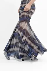 Vestido largo de microtul con estampado tipo batik en tonos azules, grises y blancos. Presenta un diseño sin mangas con cuello redondo y abertura tipo gota en el pecho. El cuerpo está completamente fruncido y forrado, mientras que la falda posee un diseño transparente con terminación en picos que aporta movimiento.