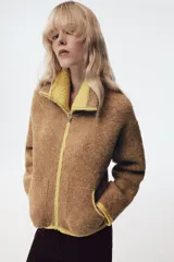 Chaqueta de punto de textura bouclé en color marrón, con cuello subido, manga larga y cierre frontal con cremallera. Presenta detalles de ribetes y acabados en color verde lima a contraste en cuello, cierre, bolsillos y puños.