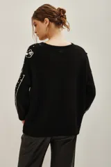 Sweater negro de punto con cuello redondo, manga larga y diseño holgado. Presenta aplicaciones de lentejuelas plateadas dispersas, bordes plateados en las mangas y apliques florales con lentejuelas en el hombro y frente.