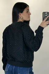 Buzo de cuello redondo y manga larga, color negro, con diseño de pequeños puntos brillantes distribuidos por toda la prenda. Presenta puños y ruedo acanalados.