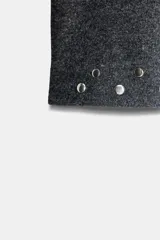 Vestido corto de punto color gris oscuro, con cuello barco y mangas largas acampanadas. Presenta detalles de tachas metálicas aplicadas en el ruedo y en los puños, con un diseño de corte evasé.