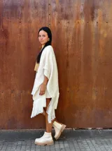 Ruana tejida de lana en color crudo, con diseño de flecos en los bordes. Es una prenda versátil y abrigada, ideal para complementar diversos looks.