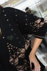 Saco de punto gris con diseño geométrico en color amarillo, cierre frontal con botones, cuello redondo y bordado de corazón pequeño en el pecho.