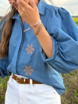 Camisa de denim azul con mangas abullonadas y detalle de flores estampadas en el frente.