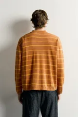Polo de punto de algodón con diseño a rayas horizontales en tonos tostado y amarillo, cuello solapa y cierre frontal parcial con tres botones. Presenta mangas largas y efecto lavado.