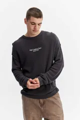 Sweater oversize de tejido liviano color gris oscuro, con hombros caídos, costuras a la vista y bordado sutil en el pecho.