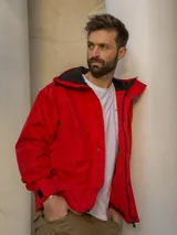 Campera rompevientos roja con capucha, cierre frontal con botones a presión y bolsillos laterales con solapa. Interior del cuello en contraste negro.