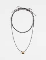 Collar largo de cordón negro ajustable, con dije metálico irregular en tono dorado.