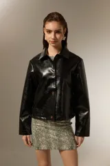 Chaqueta de eco-cuero negro con acabado brillante, cuello camisero, cierre frontal con botones y mangas largas.