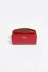 Billetera compacta de cuero vacuno color negro, con cierre superior metálico dorado y logo de la marca estampado en el frente.