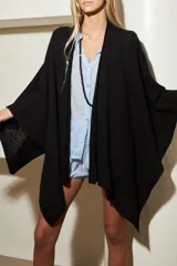 Ruana o poncho de tejido de punto negro, con textura suave y diseño envolvente de corte asimétrico.