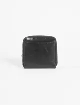 Billetera pequeña de cuero vegano color lila claro, con cierre perimetral de cremallera y tirador metálico. Presenta un logo metálico en bajo relieve en el frente.