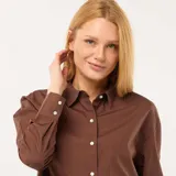 Camisa de manga larga de popelina color marrón, con cuello camisero, cierre frontal de botones y puños anchos.