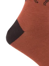 Calcetines de caña media color ladrillo con detalles en marrón oscuro en la puntera, el talón y el borde superior. Presentan un diseño de paisaje montañoso en tonos grises y negros, y un logo de Puma en la parte superior.