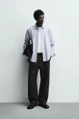 Camisa de corte regular fit confeccionada en tejido de algodón con diseño de rayas verticales. Presenta cuello abotonado, manga larga con puños abotonados, bolsillo plastrón en el pecho y cierre frontal con botones.