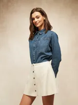 Falda corta de gamuza sintética en color beige, con diseño de paneles verticales y cierre frontal mediante botones metálicos a presión.