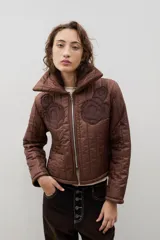 Campera crop acolchada color marrón, con cuello alto, cierre frontal y apliques de flores en el pecho. Presenta un diseño capitoneado y forro interior.